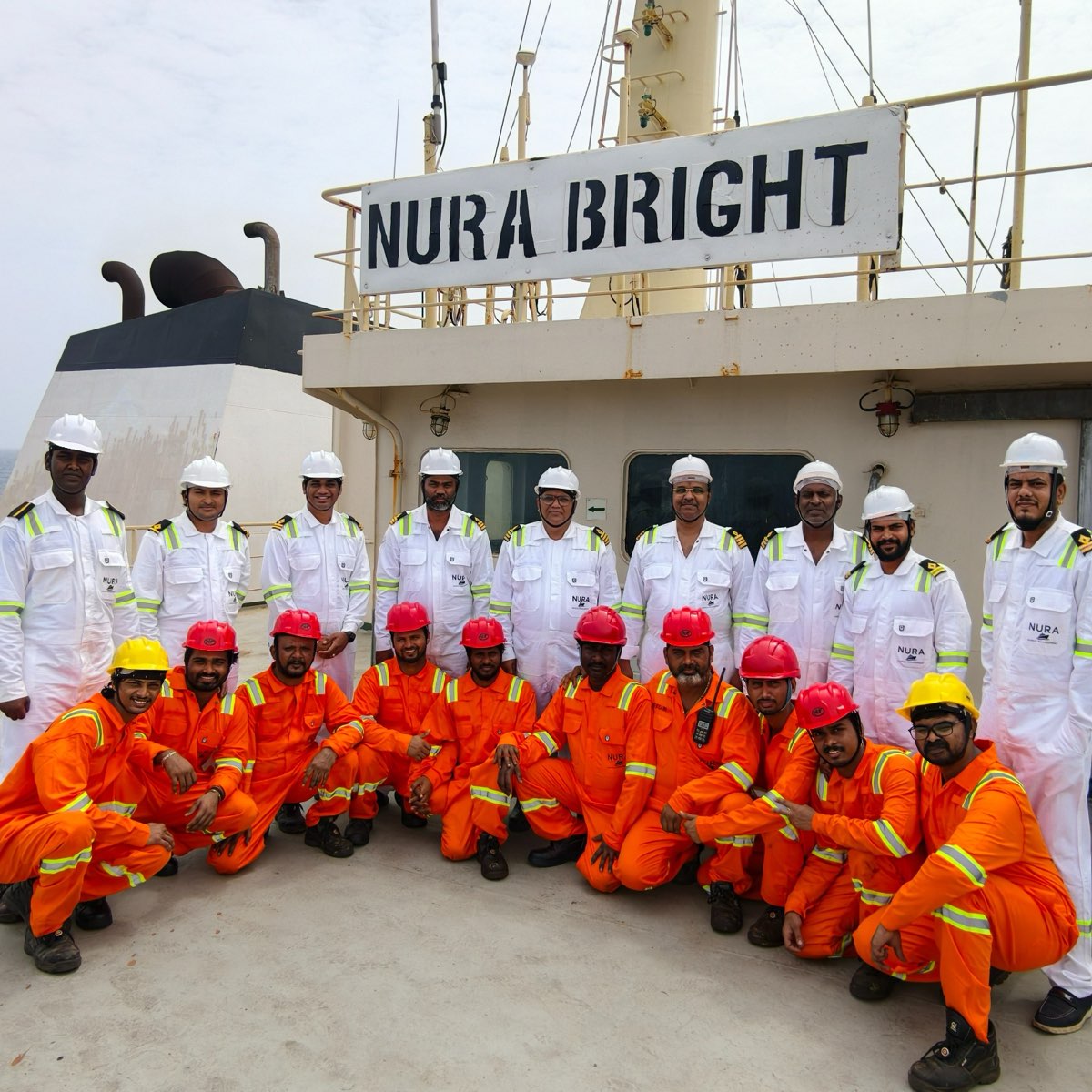 The crew of the NURA BRIGHT in NURA uniforms, gathered on deck beneath her name board